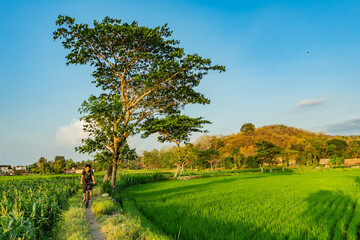 Happy young asian man wearing a backpack enjoying late afternoon mountain bike ride through the forest by river on a clear day