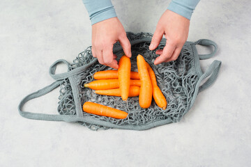 Unpack fresh carrots from a reusable grocery mesh bag, vegetables from the market, healthy food and...