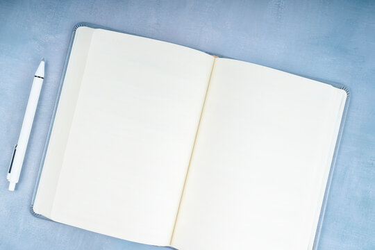 Blank open book and pen on blue wooden background.