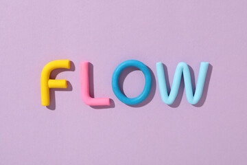 The word "flow" is laid out from colored plasticine on a purple background.