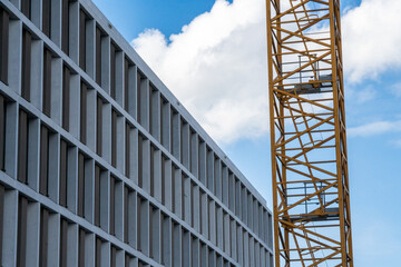 Facade of a new building. Office building with many windows next to a construction crane. Blue sky with white clouds