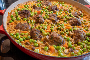 Meatball kritharaki pan with peas and carrots in the cast iron pan. One-pot dish