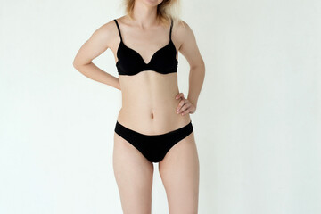 Unretouched skinny white young woman, slim body in black underwear on studio white wall background,...
