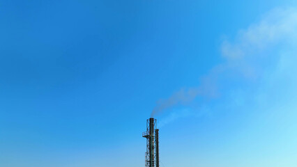 A factory's chimney releases black smoke into the serene blue heavens, a poignant reminder of air...