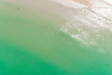 zenithal aerial drone view of two people in turquoise water on the shore of a beach enjoying the...