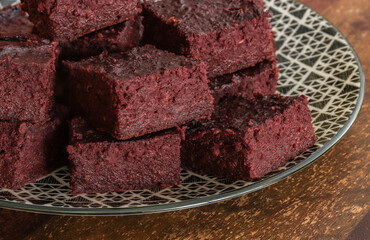 Moist beetroot brownies on a patterned plate with wooden table background.