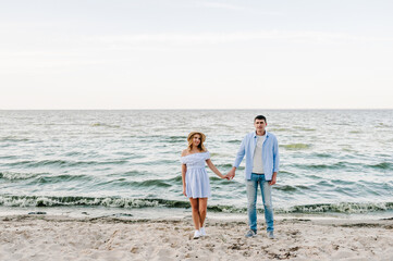 Couple in love holding hands and looking at camera on seashore sea. Man and woman on sand. Female and male standing on beach ocean and enjoying sunny summer day on vacation. Spending time together