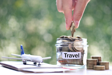 Stack of coins money in the glass bottle and airplane on passport with natural green...