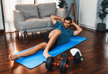 Athletic and sporty man doing crunch on fitness mat during home body workout exercise session for...