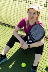 Young female smiling and looking at camera while playing padel against green background  - 796325749