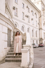 woman in elegant coat and hat against an intricate architectural backdrop, harmoniously blending modern fashion with historical allure. The soft daylight adds to its timeless appeal.