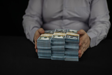 On a black background, a man in a business shirt moves wads of dollars at the camera. A man holds...