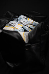 Vertical. An unzipped bag with money in one hundred dollar bills on a black background close-up. Stacks of new hundred dollar bills were placed in a black bag for transportation.