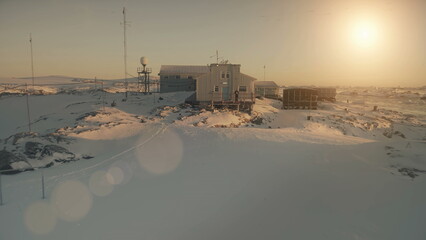 Close-up Vernadsky base and man. Antarctica aerial drone view flight. Fast Antarctic snow covered landscape. Camp, base building with walking man. Sunset polar sky. Permafrost. © mozgova