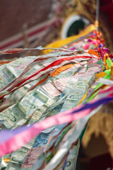 Thai banknotes attached to a rope flutter in the wind in a Buddhist temple, close up