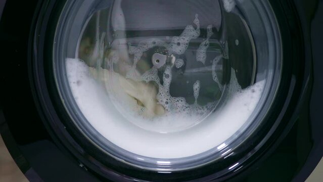 Fast spinning washing machine drum rotating dirty clothes with water during laundry at home