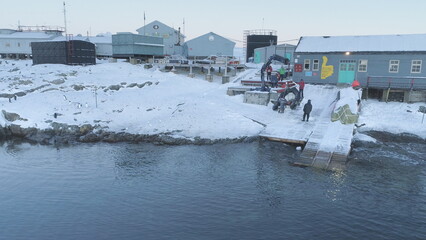 People work on pier of Antarctic polar station - Vernadsky. View of robotic arm pulls out boat....