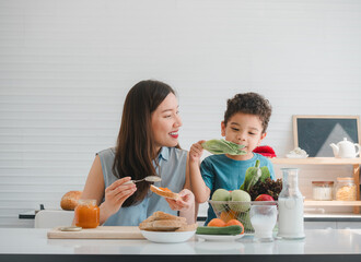Happy young Asian mother and son make bread with jam for breakfast together in the kitchen at home. Family Cooking concept.