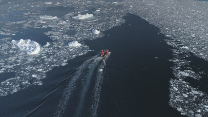 Zodiac motor boat sailing in Antarctic ice. Aerial tracking - drone flight overview of south pole ocean landscape. Rubber boat float in winter open water brash ice. - obrazy, fototapety, plakaty