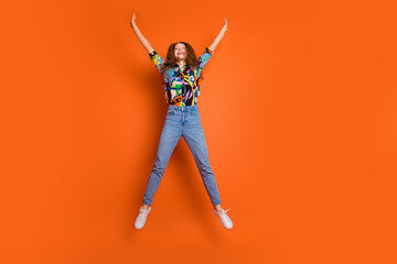 Photo of overjoyed funny cute girl wear trendy print clothes jump up raised hands isolated on orange color background