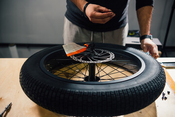Closeup view of new motorcycle wheel lies on the table in the workshop. The craftsman is holding...