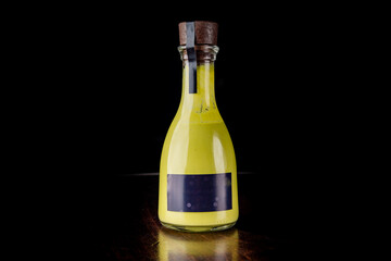 Vintage bottle with yellow liquid, sealed with a cork and labeled with a blank dark sticker, isolated on a black background