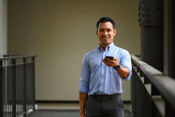 Confident businessman using mobile phone standing in the office corridor
