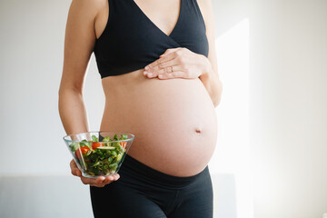 Pregnant woman's belly and vegetable salad. Prenatal nutrition during pregnancy.