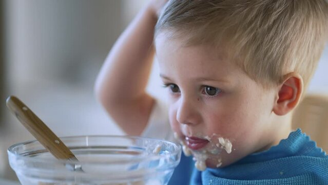 Baby eats cereal porridge. Bboy is holding spoon in his hand. Child sits at table and eats porridge.Family breakfast in kitchen. Feeding child at table.Child proper nutrition.Breakfast in kindergarten