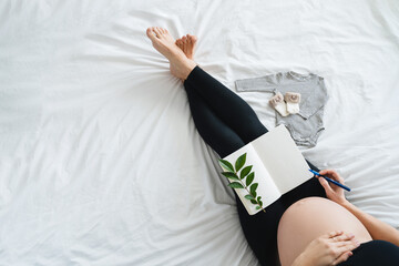 Pregnant woman with beautiful belly makes notes or check list in paper diary.
