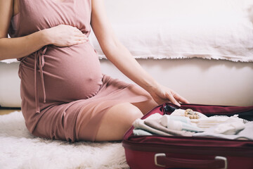 Close-up belly of pregnant woman with travel bag of clothes and necessities. Mother during pregnancy preparing and packing suitcase for maternity hospital getting ready for baby birth.