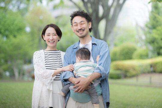 新緑の屋外で赤ちゃんを抱っこして微笑むミドル層の家族