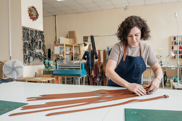 Caucasian woman makes belts from genuine leather in a workshop. 