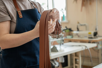Close-up of a Caucasian woman's hands making genuine leather belts in a workshop. 