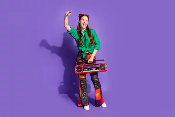 Rolgordijnen Full size photo of cool nice woman dressed green shirt print trousers hold boombox raising palm isolated on purple color background © deagreez