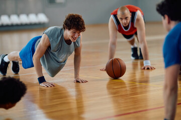 Happy basketball players doing push-ups during sports training at indoor court.