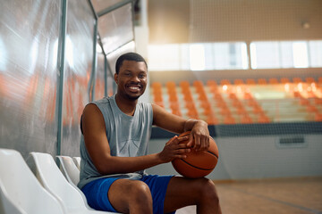 Happy black player with  ball during basketball practice looking at camera.