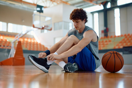 Young basketball player tying shoelace on court.