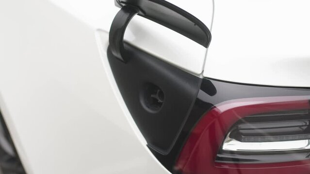 Hand-held shot of a woman's hand charging an electric car at an outdoor charging station against the background of a business center of a European street. Zero emission vehicle.