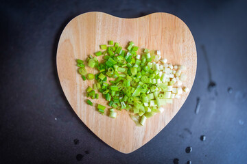 Chopped onion leeks on the heart shaped wooden board