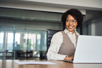 Happy young African American professional business woman bank worker or hr manager, corporate employee looking away at work working on laptop computer in office thinking of future career. Copy space.