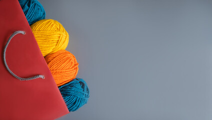 Flat lay of colorful balls of yarn inside a recycled paper bag over a gray table