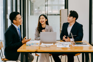 Group of businesspeople are sitting around a table in a business setting. They are all smiling and seem to be enjoying each other's company