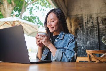 Portrait image of a young woman drinking coffee while working on laptop computer in cafe - 796412130