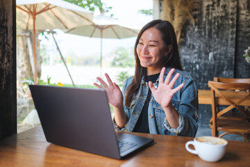 Portrait image of a young woman using laptop computer for video call, online meeting in cafe