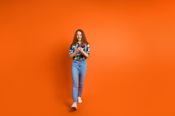 Photo of adorable nice girl blogger dressed trendy clothes going street chatting isolated on orange color background