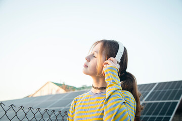 A girl listens to music on headphones against the backdrop of solar panels.