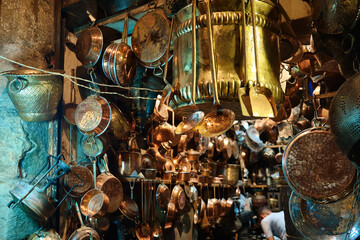 Copper handicrafted jugs, plates and other tableware hanging in a traditional middle eastern market. Brass tableware shop