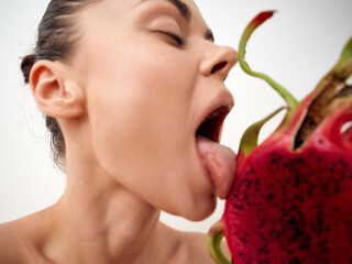 Playful woman sticking out tongue with exotic dragon fruit in front of mouth, healthy eating concept
