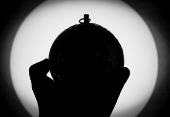 silhouette of hand holding disco ball against light source